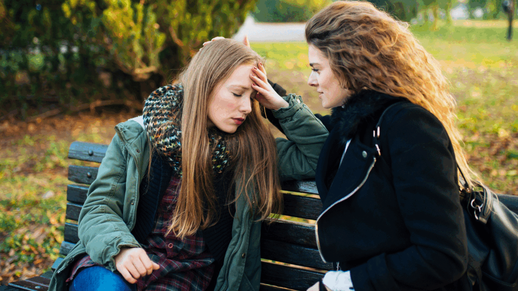 Two Girls  Sitting On bench Asking each other How are you Feeling today.
