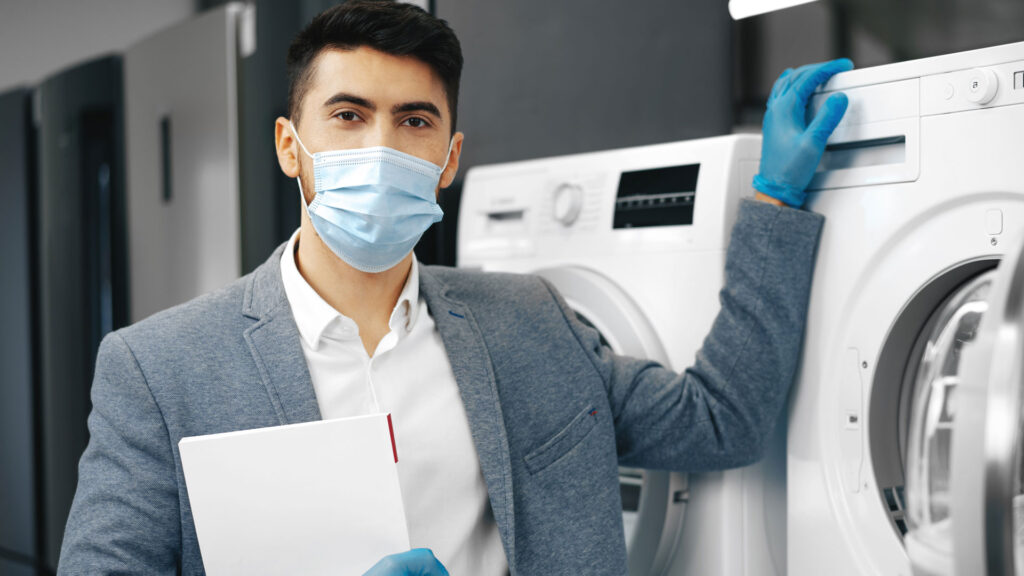 Professional Dry Cleaner wearing gloves and mask  Standing Infront Of Washing Machine.